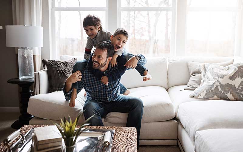 Bilden visar en pappa med sina två söner som klättrar på hans rygg och skrattar